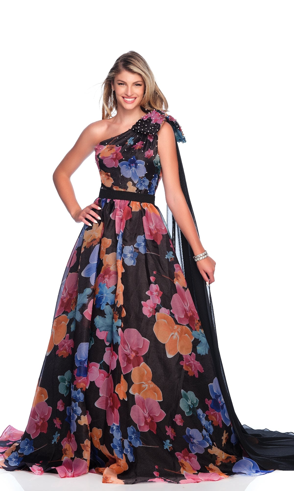 A woman smiles in the Dave & Johnny 12157 Floral Print Prom Dress, featuring an elegant one-shoulder neckline and a long sheer black train, posing against a plain white background.